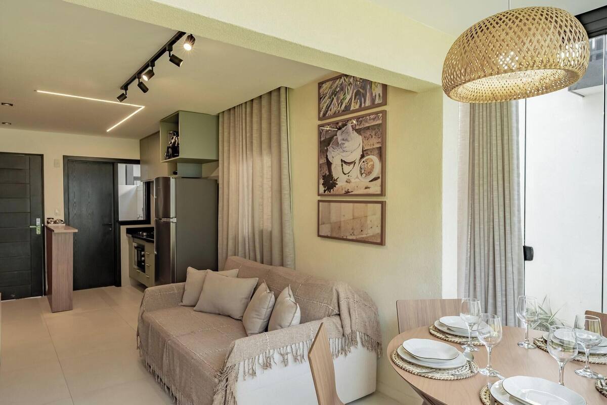 A modern living room with a sofa, dining table set for six, and a kitchen area with a refrigerator.
