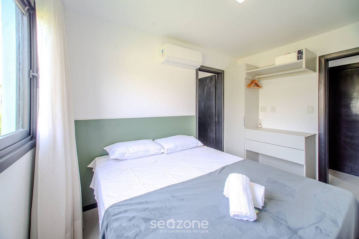 A hotel room with a bed, an air conditioning unit, a wardrobe, and a window with curtains.