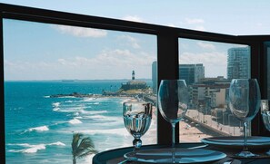 A table set with wine glasses and plates, overlooking a coastal view with a lighthouse and buildings.