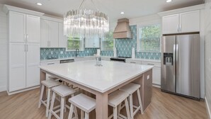 Una cocina moderna con armarios blancos, una isla grande con taburetes, un refrigerador de acero inoxidable y una lámpara decorativa.