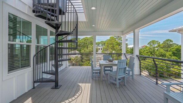 Una terraza techada al aire libre con una escalera espiral, una mesa con sillas y vistas a árboles y edificios.