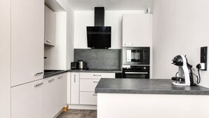 Een moderne keuken met witte kasten, een zwarte afzuigkap, een koffieapparaat en een magnetron.