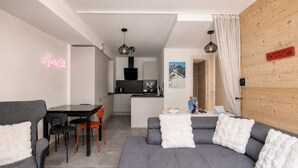 Een moderne woonkamer met een grijze bank, een eettafel met stoelen, een keukenhoek, en een neonreclame.