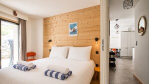 Een hotelkamer met een houten hoofdeinde, een bed met witte lakens, twee opgerolde handdoeken, een kleine oranje stoel en uitzicht op het exterieur.