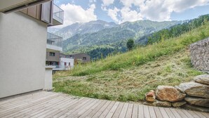 Een houten terras met uitzicht op bergen en een gebouw met balkons.