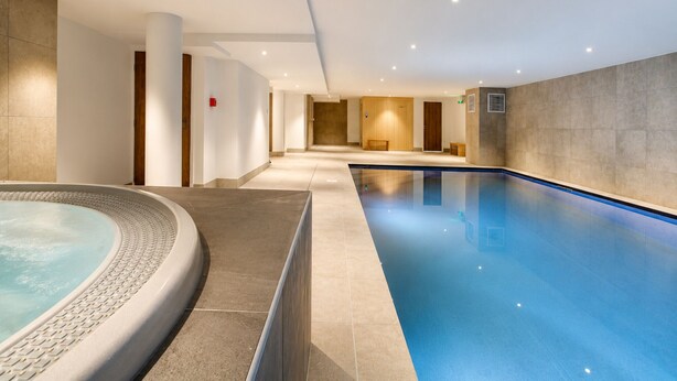 Een zwembad met een jacuzzi, betegelde muren en inbouwverlichting.