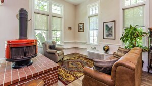 A cozy living room with a brick fireplace, comfortable seating, large windows, and a decorative rug.