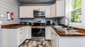 A compact kitchen with white cabinets, a microwave, an oven, a sink, and a wooden countertop.