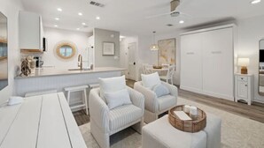 A modern, well-lit living area with a kitchen, two striped armchairs, a dining table, and a large white wardrobe.
