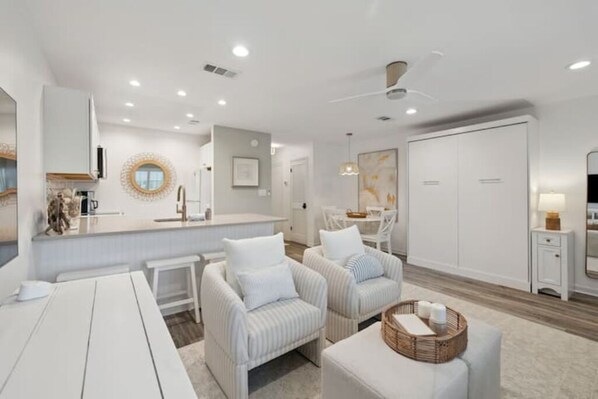 A modern, well-lit living area with a kitchen, two striped armchairs, a dining table, and a large white wardrobe.