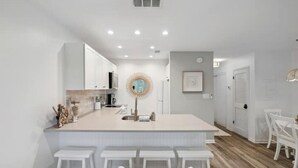 A modern kitchen with white cabinetry, a central island with bar stools, and a dining area with white chairs.