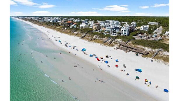 A beach with houses along the shore, clear skies, and people on the sand.