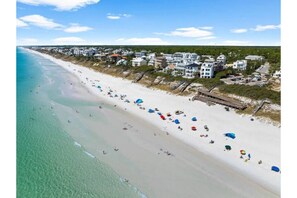 A beach with houses along the shore, clear skies, and people on the sand.