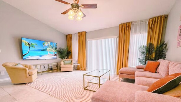 Una sala de estar con sofá, sillón, mesa de centro y televisor en la pared.