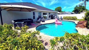Una piscina con un flotador de flamenco rosa, rodeada de follaje y un patio cubierto con muebles de exterior.