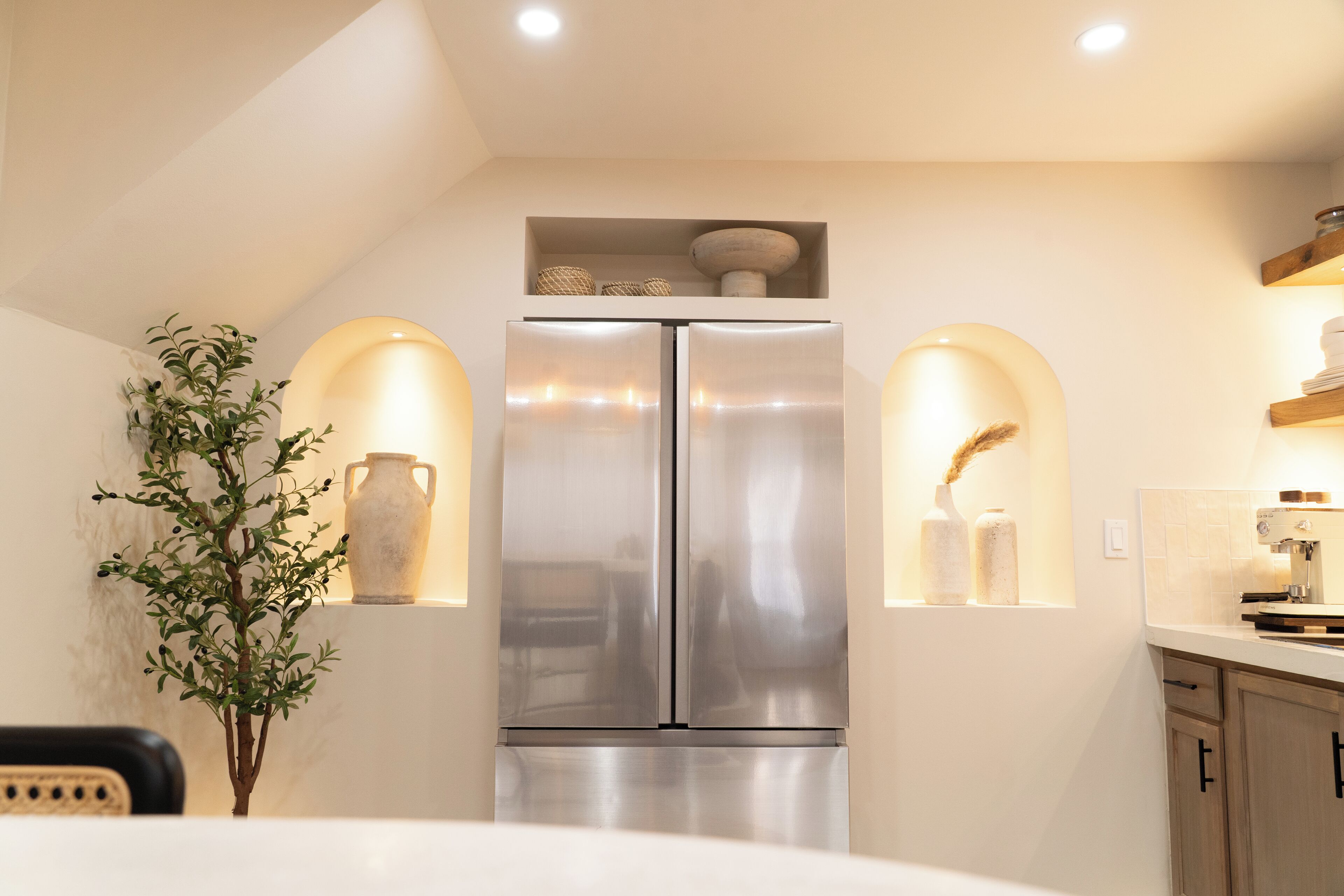 A modern kitchen with a stainless steel refrigerator, two wall-mounted lights, and a small plant.