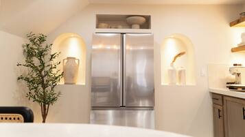 A modern kitchen with a stainless steel refrigerator, two wall-mounted lights, and a small plant.