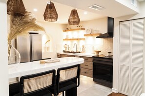 Une cuisine moderne dotée d’un îlot central, de chaises noires, de luminaires suspendus en osier et d’un four encastré.