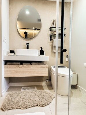 Une salle de bain moderne avec un miroir rond, un lavabo blanc et des carreaux de couleur beige.