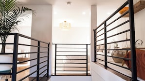 Una escalera moderna con barandilla de metal negro, una lámpara colgante y una planta en maceta.