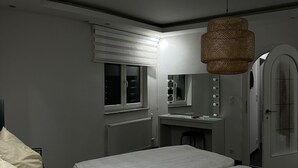 A bedroom with a bed, a vanity with a mirror, a hanging light fixture, and a door.