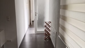 A narrow hallway with dark tiled flooring, white walls, and a door at the end.