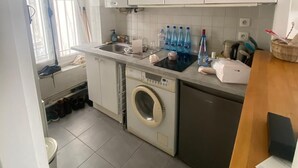 A compact kitchen with a washing machine, a sink, and a countertop with bottles. - Studio Rue Charlot, Marais (quartier marché des enfants rouges) (Paris)