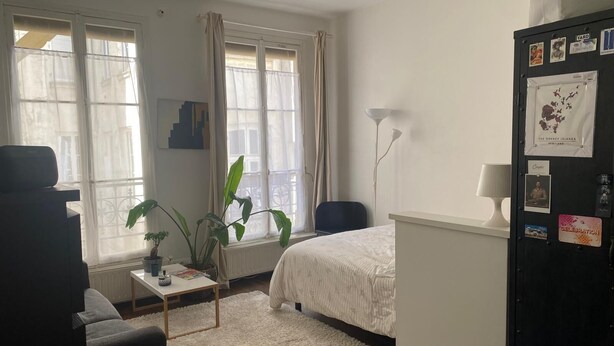 A hotel room with a bed, a desk with a laptop, a chair, a small table with a plant, and a window with curtains. - Studio Rue Charlot, Marais (quartier marché des enfants rouges) (Paris)