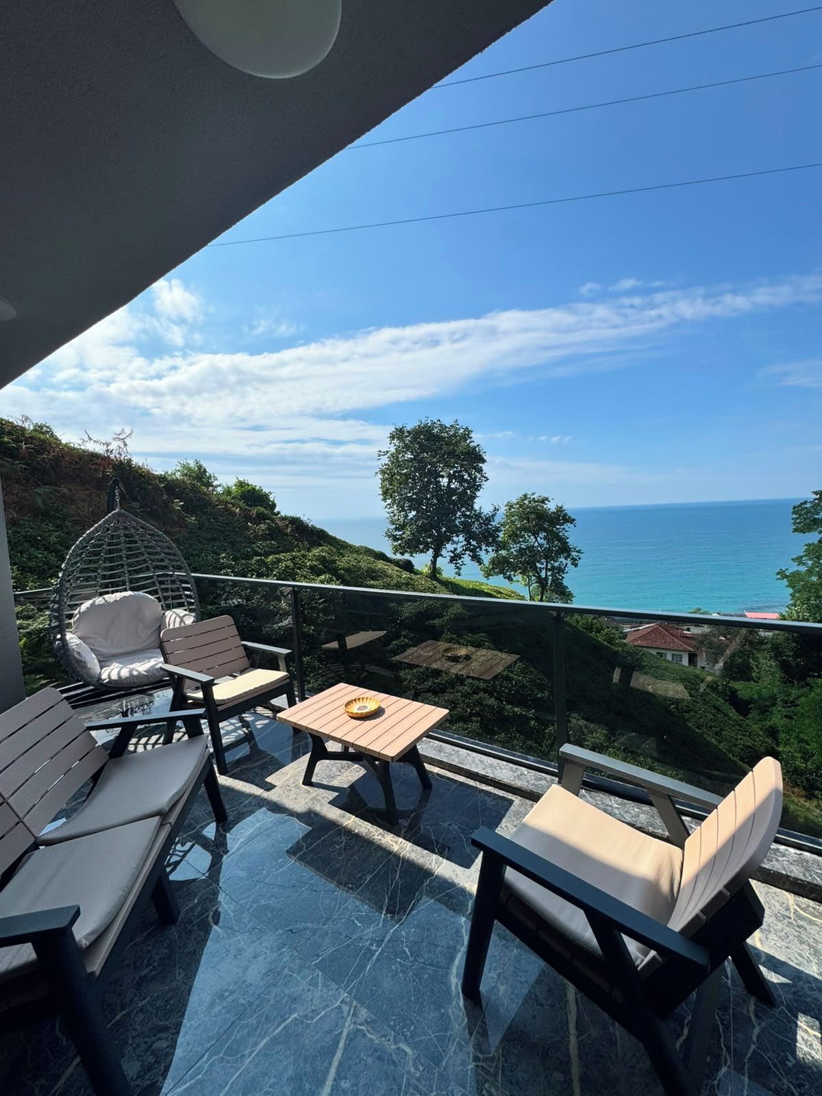 Un balcon avec vue sur la mer, du mobilier d’extérieur et un ciel dégagé.