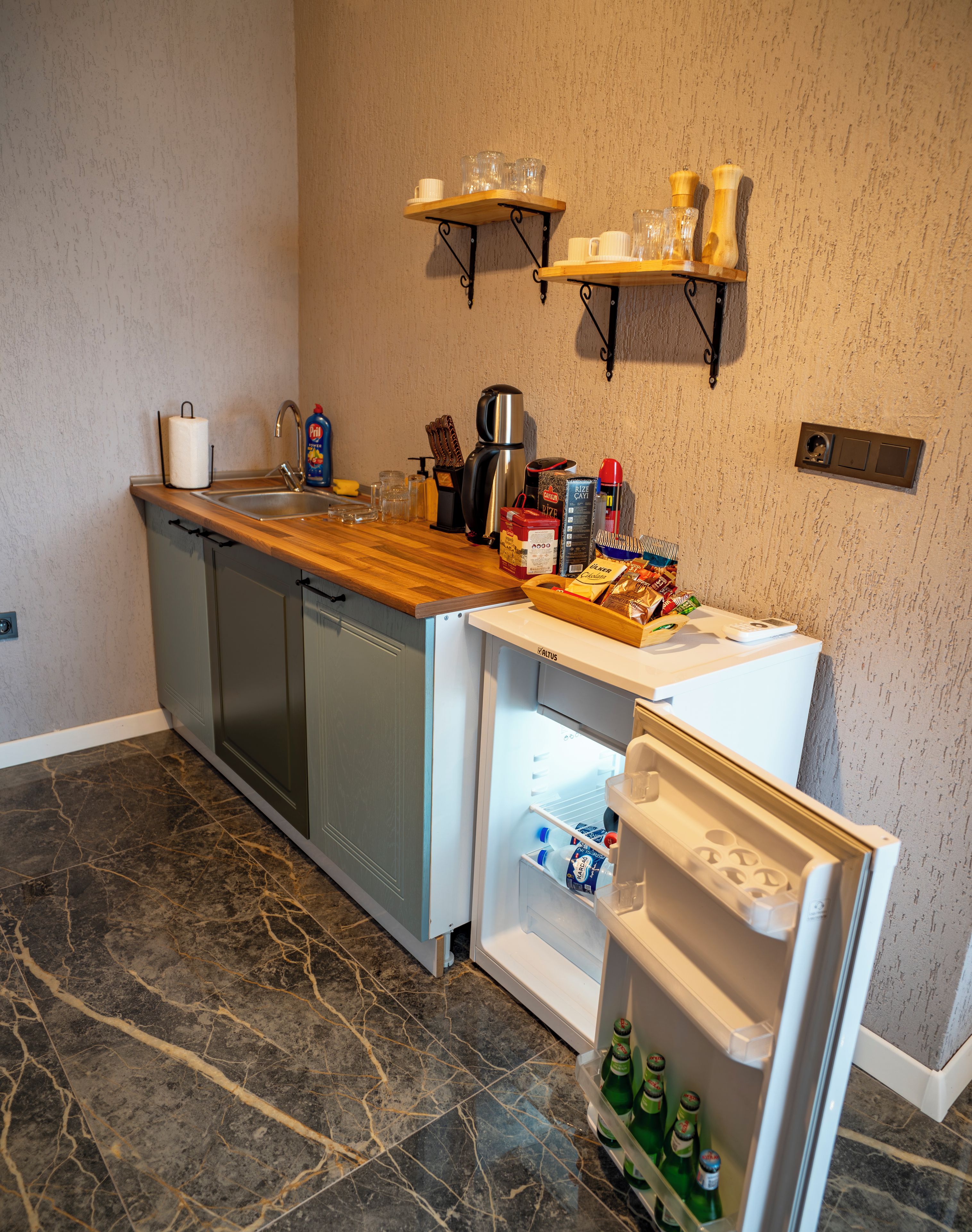 A kitchen with a dishwasher, a refrigerator, a wooden countertop, and a wall-mounted shelf with glasses.