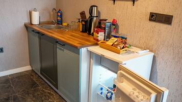 A kitchen with a dishwasher, a refrigerator, a wooden countertop, and a wall-mounted shelf with glasses.