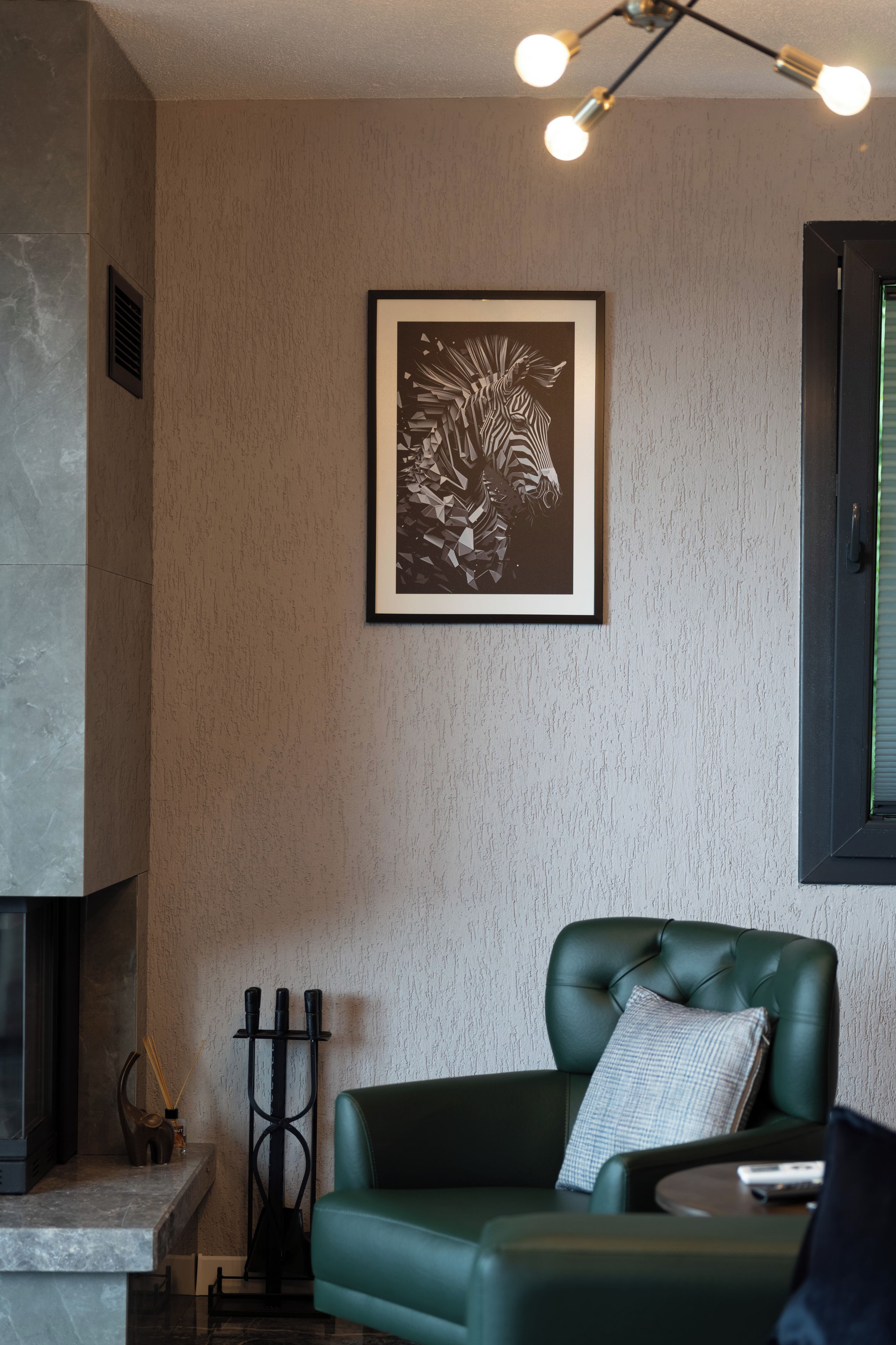 A room with a green leather sofa, a framed abstract artwork, a fireplace, and a window with blinds.