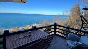 Una terrassa de fusta amb taula i cadires, una cadira penjant i vista a l'oceà.