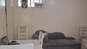 A living room with a grey sofa, a white table with a laptop, a black rug, and a ceiling fan.