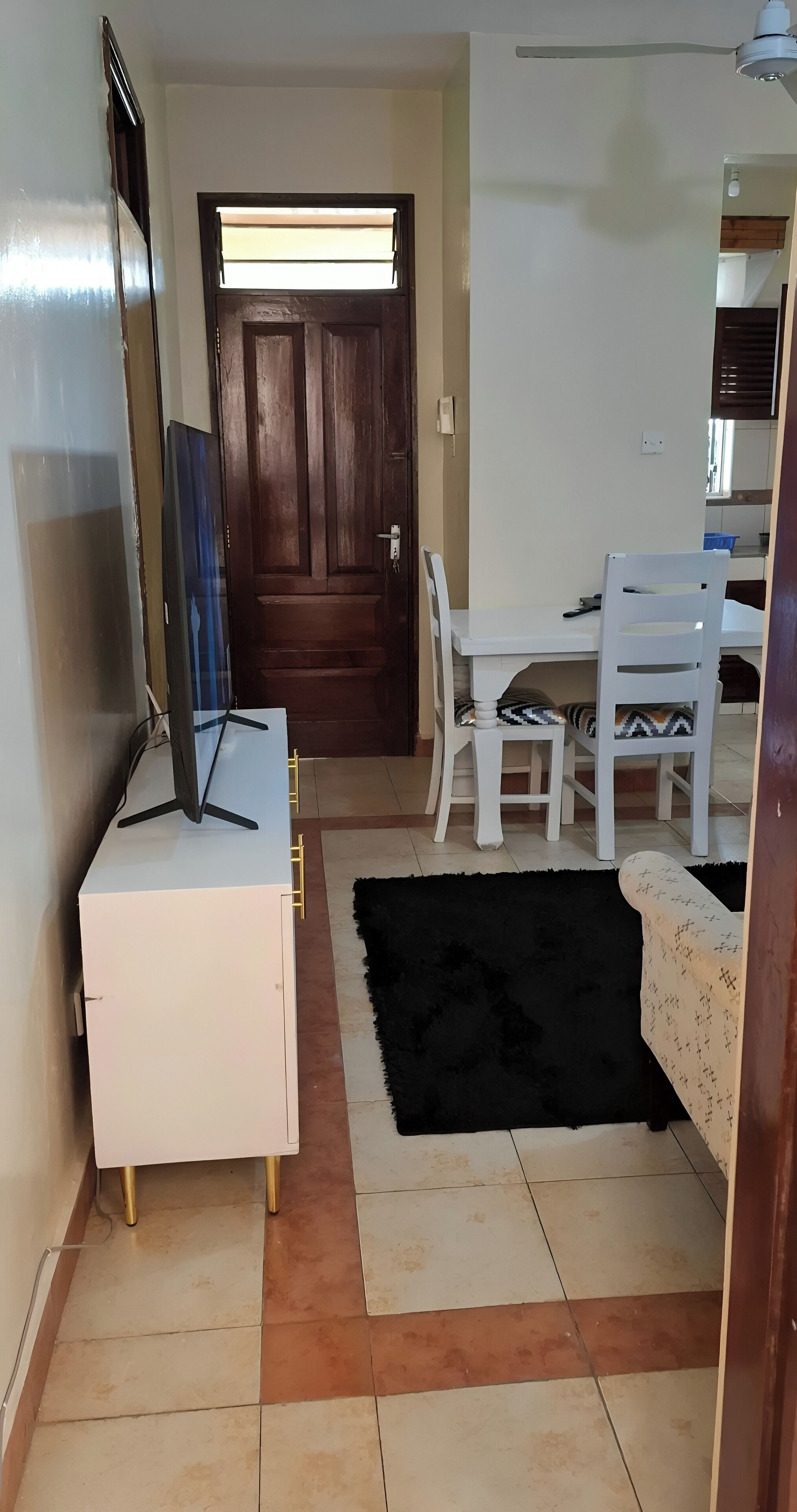 Un espacio habitable compacto con un escritorio blanco, un televisor, un tapete negro y una puerta de madera.