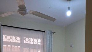 A bedroom with a bed, a ceiling fan, a window with a curtain, and a light fixture.