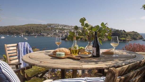 A wooden table with a view of a coastal town, a bottle of wine, and a glass of white wine. - Dolly's Plaice -  a cottage that sleeps 4 guests  in 2 bedrooms (Fowey)