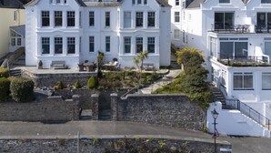 A row of white, two-story houses with large windows and a stone wall in the foreground. - Dolly's Plaice -  a cottage that sleeps 4 guests  in 2 bedrooms (Fowey)