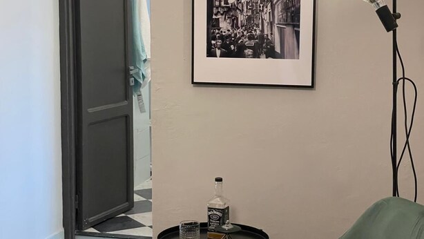 A hallway with a framed black and white photograph on the wall, a green chair, a small table with a bottle and glass, and a floor lamp. - The Coccagna Hideaway Secret Whispered in the Alleys (Genova)