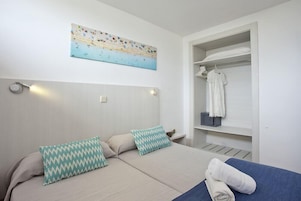 Un dormitorio con dos camas, un cuadro de una playa, un armario y una toalla sobre la cama.