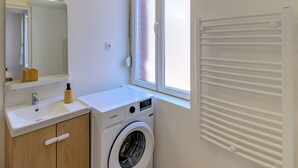 A modern bathroom with a white sink, mirror, and a front-loading washing machine. - Delmas - 5min Centre Ville - Wifi (Saint-Quentin)