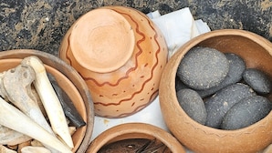 Een verzameling traditionele gereedschappen en materialen, waaronder een vijzel en stamper, een schaal met stenen en een schaal met gedroogde vis, uitgestald op een doek.