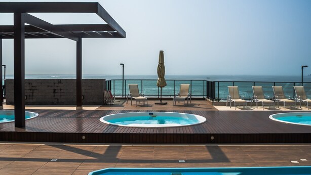 Zona de piscina en la azotea con sillones de descanso y un jacuzzi, con vistas al mar.