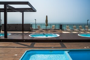 A rooftop pool area with lounge chairs and a hot tub, overlooking the sea. - VAC - Beachfront Condo in Itajuba Beach (Barra Velha)