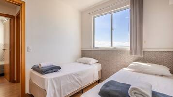 Une chambre avec deux lits, une fenêtre avec des rideaux et une porte donnant sur une autre pièce.