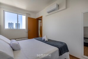 Ein Hotelzimmer mit großem Fenster, einem Bett mit weißen Leinen, einer grauen Decke und einem Handtuch auf dem Bett.