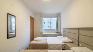 A hotel room with two beds, a window with curtains, a mirror, and a view of buildings outside.