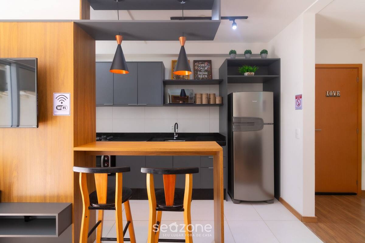 Uma cozinha moderna com uma ilha de madeira, banquetas pretas, geladeira de aço inoxidável e luminárias pendentes.