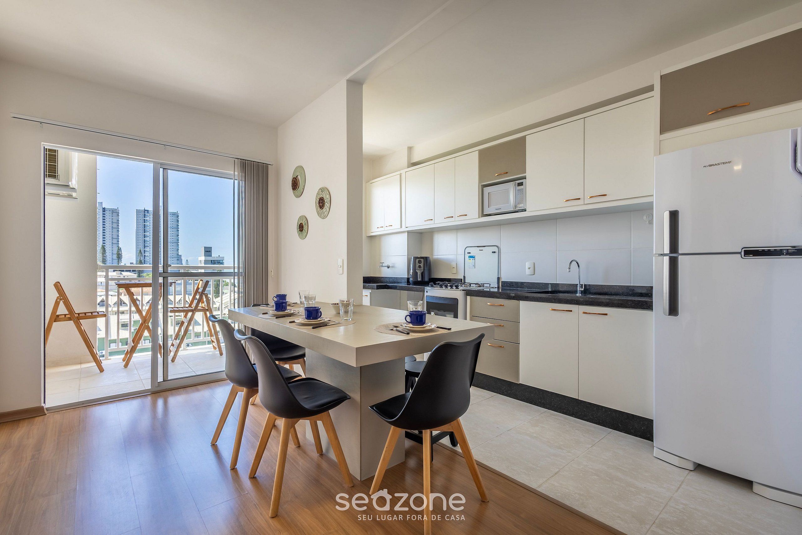 Una cocina moderna con una isla central, armarios blancos y un amplio ventanal con vistas a un paisaje urbano.