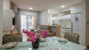 Una sala de estar moderna con una mesa de comedor de vidrio, un sofá y una cocina con armarios blancos.